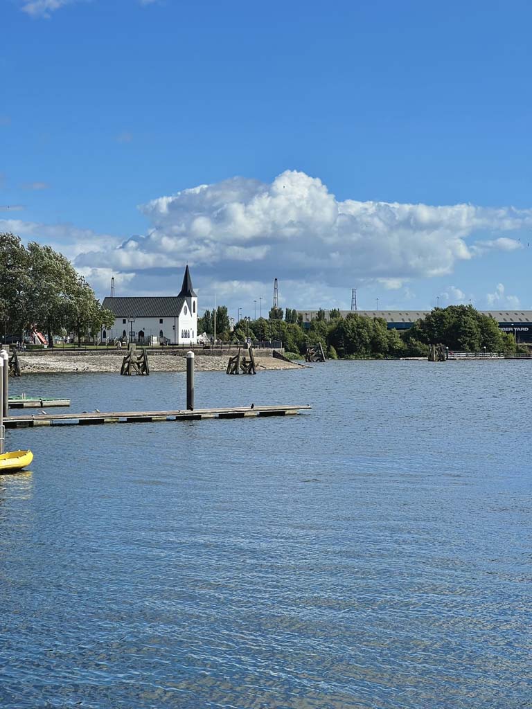 A jetty over blue water with a white church in the distance