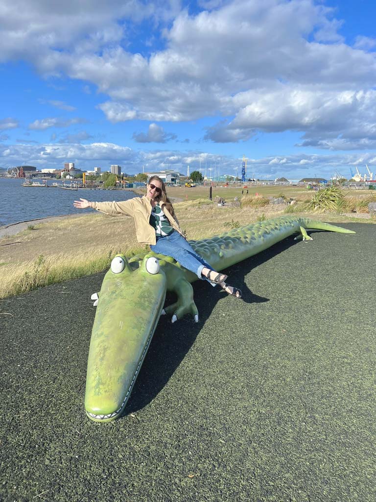 A woman sitting smiling on a large crocodile sculpture